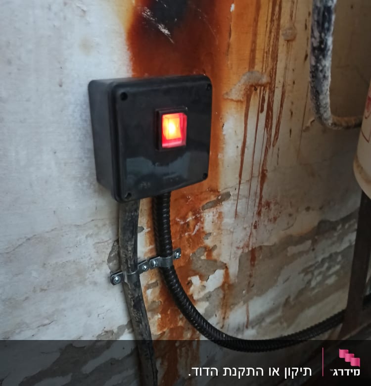 מתג עם נורית אדומה על קיר חלוד